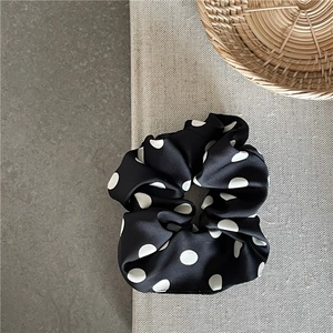 Detail view of a large black satin scrunchie with classic white polka dots on textured fabric