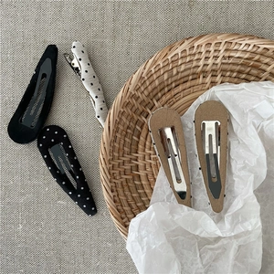 Close-up of five minimalist black and white polka dot fabric hair clips on a woven tray