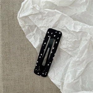 Détail d'une pince à cheveux rectangulaire en tissu noir à pois blancs avec clip BB