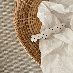Polka dot fabric hair clip with black and white wavy pattern on a rustic straw tray