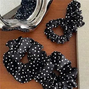 Elegant black scrunchie with white polka dots on a stylish wooden background
