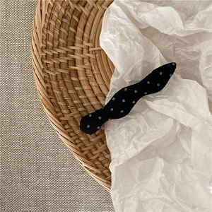 Detailed view of a wave-shaped black fabric hair clip with white polka dots for hair styling
