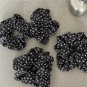 Detail of four black polka dot scrunchies with pleated fabric texture on gray surface