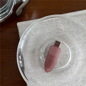 Detailed view of a matte dusty rose teardrop hair clip on a glass dish and linen cloth