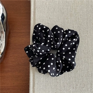 Detailed view of black polka dot scrunchie placed on a beige fabric book cover