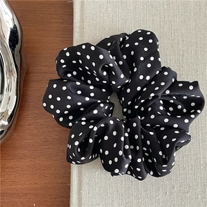 Close-up of black satin scrunchie with white polka dots on a wooden background