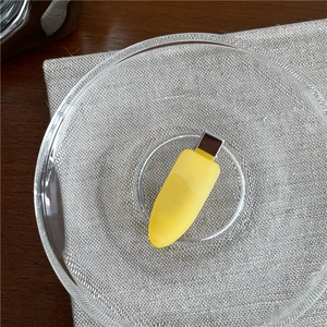 Vertical top view of a ginger yellow teardrop hair clip on a clear glass plate