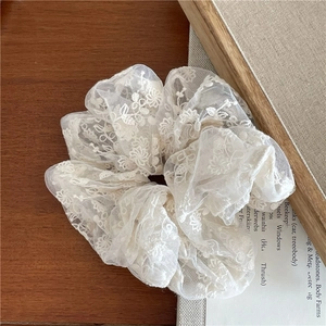 Gros plan d'un chouchou en dentelle blanc cassé avec broderie florale sur tissu en maille