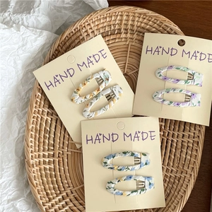 Close-up of three pairs of floral fabric-wrapped hair clips in yellow, purple, and blue