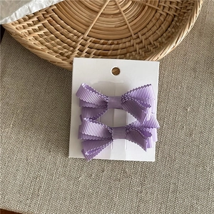 Dettaglio di due fermagli per capelli a fiocco viola in nastro su cartoncino bianco