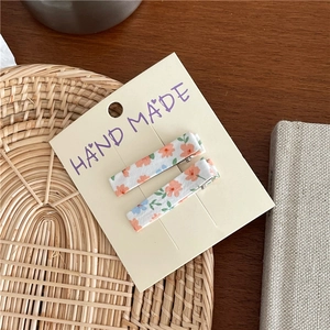 Close-up of handmade floral fabric hair clips set on cardboard against a wooden table