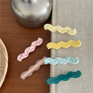 Détails de barrettes ondulées en acétate aux couleurs variées sur un support en bois