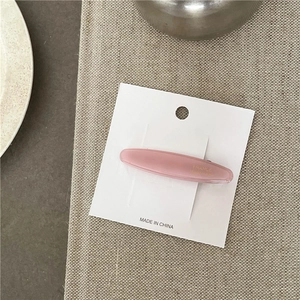 Detailed macro view of a handmade pink acetate oval hair clip on a white display card