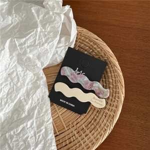 Détail de barrettes à cheveux ondulées en acétate marbré et blanc crème sur carte