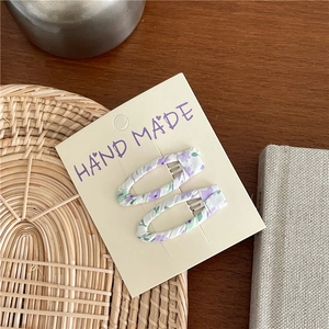 Set of two handmade purple floral fabric clips on a white card display over wood