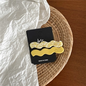 Détail de barrettes ondulées en acétate jaune et marbré sur une carte de présentation