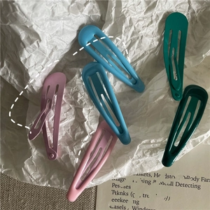 Close-up of matte pastel metal BB hair clips in pink and green on a textured fabric