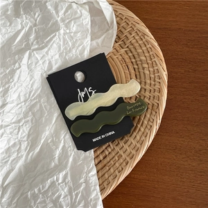 Détail de barrettes à cheveux ondulées en acétate crème et vert forêt sur carte noire