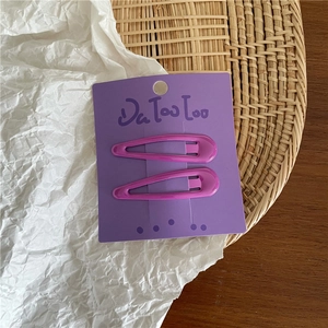 Macro detail of two purple cream metal teardrop hair clips on a purple display card