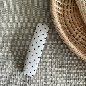 Detailed view of rectangular hair clip with black and white polka dot fabric on linen