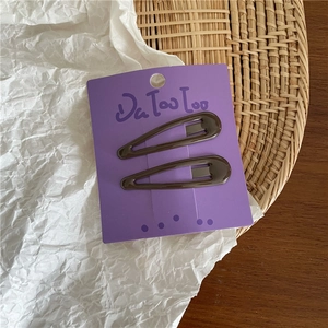 Detail of two dark brown cream-colored metal teardrop hair clips on purple card