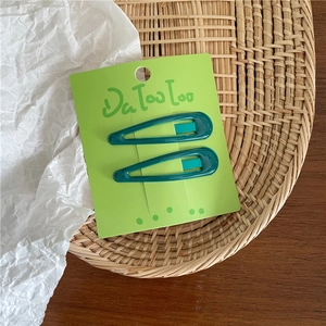 Close-up of two dark green teardrop BB hair clips on a light green display card