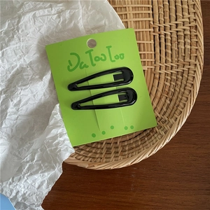 Close-up of two black glossy water-drop BB hair clips on a green display card