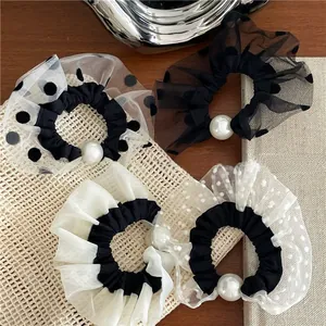 Detailed view of mesh polka dot scrunchies featuring decorative faux pearls on a beige surface