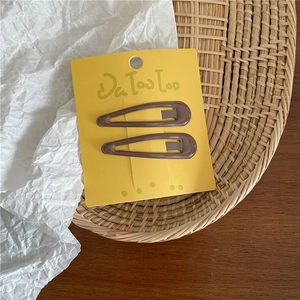 Detail of two coffee brown water-drop BB hair clips on yellow card over woven tray