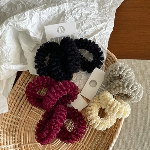 Detail of mesh fabric scrunchies set in black, burgundy, and beige on a woven tray