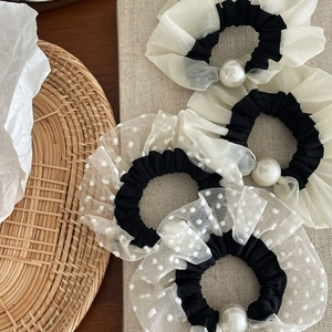 Detailed view of four mesh polka dot scrunchies with white pearls on a textured board