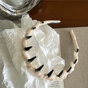 Dettaglio del cerchietto beige intrecciato decorato con borchie a punta nere lucide