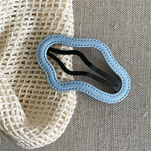Close-up of wavy denim blue fabric hair clip on rustic beige linen background