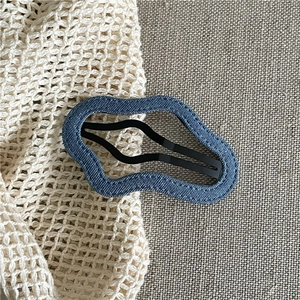 Close-up of wavy blue denim fabric hair clip with black matte metal snap fastener