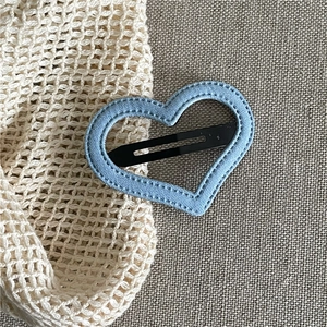 Close-up of heart-shaped denim hair clip with white stitching on beige linen background