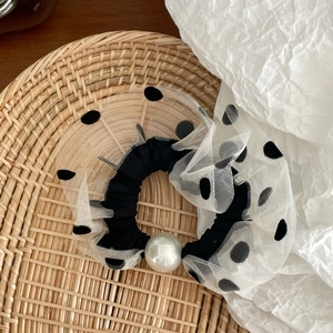 Close-up of black mesh polka dot scrunchie with a large white pearl detail on woven basket