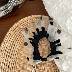 Detail of white polka dot mesh hair scrunchie placed on a textured rattan tray