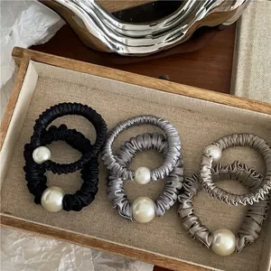 Elegant satin scrunchies with large pearls in black, silver, and gold on a tray