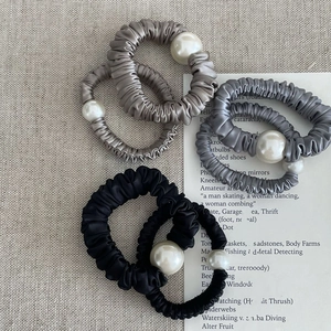 Detailed view of satin silk scrunchies featuring a large faux pearl bead and soft texture