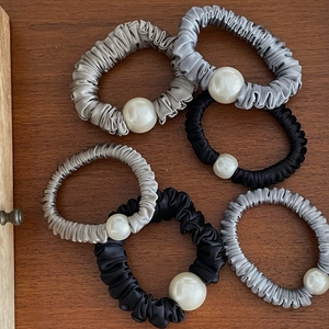 Close-up of satin scrunchies in black and grey with elegant faux pearl beads on wood