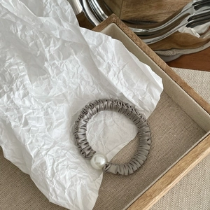 Detail view of a gray satin scrunchie featuring a large faux pearl on a wooden tray