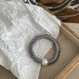 Detail of grey satin hair scrunchie with large faux pearl on a wooden tray with paper
