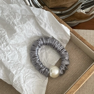 Detailed view of grey satin scrunchie with a large white pearl bead on wood tray
