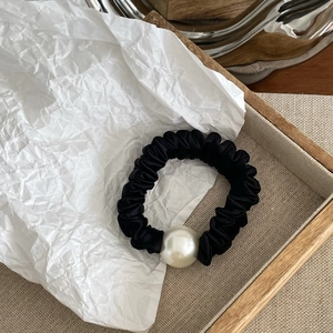 Detailed view of a black satin scrunchie featuring an elegant white faux pearl ornament