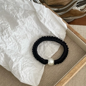 Detail of a black satin scrunchie featuring a large white pearl bead on a wooden tray