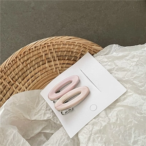 Détail de deux barrettes ovales roses en acétate sur une carte blanche avec décor en osier