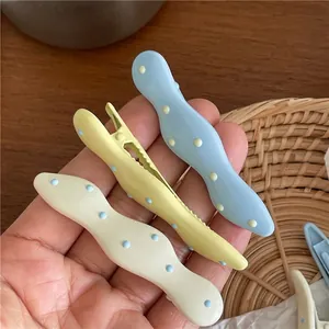 Hand holding three cream colored wavy polka dot hair clips in blue yellow and white