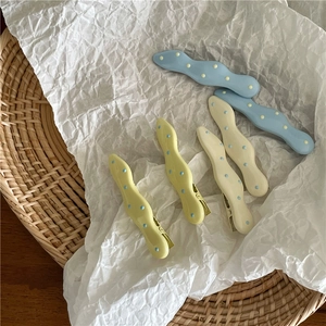 Detailed view of wave-shaped polka dot hair clips in blue, yellow and cream white