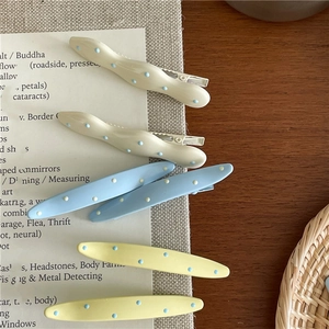 Detailed view of six cream-colored wave hair clips with blue polka dots on rustic wood