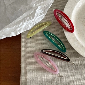 Oval rhinestone hair clips in five colors displayed on textured linen fabric